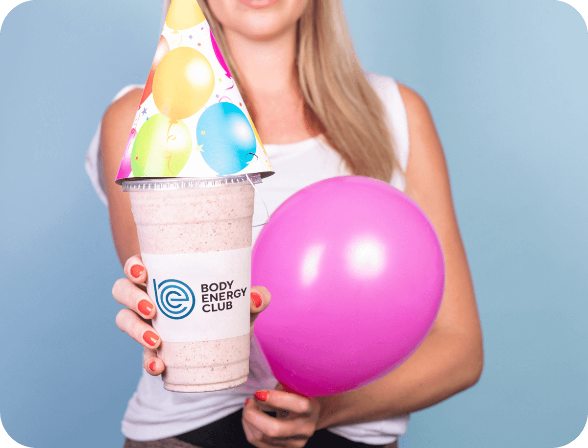 Woman holding a free birthday smoothie, a pink balloon and a birthday hat.