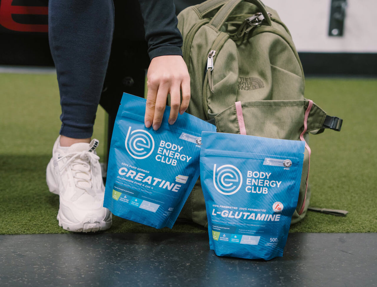 Person bending down picking up a bags of Body Energy Club Creatine and Body Energy Club L-Glutamine